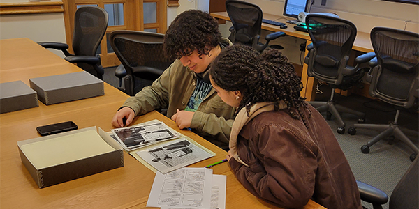 Two people are seated at a table looking at archival photographs.